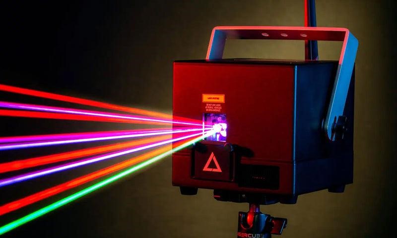 9 Lasercube laser projector closeup on a dark background with yellow halo around it, with laser lights projected out from the front.
